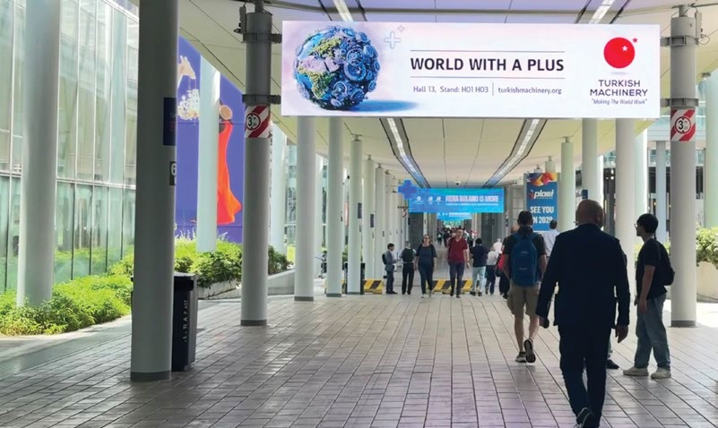 PLAST Milano fuar alanı koridorunda Turkish Machinery 'World With A Plus' bannerı ve ziyaretçiler