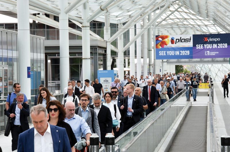 PLAST Milano 2026 fuarında yürüyen bant üzerinde yoğun ziyaretçi akışı, plast ve Xylexpo 'see you' bannerları