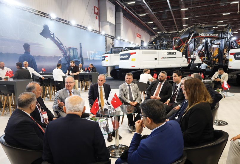 KOMATEK 2026'da İMDER standında düzenlenen uluslararası forum ve ikili görüşmeler, arka planda HİDROMEK iş makineleri