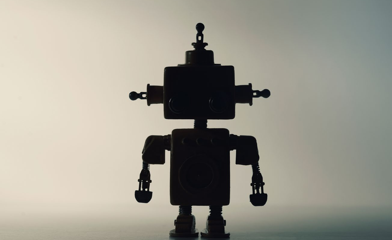 Karanlık zeminde siluet hâlinde duran küçük oyuncak robot - gölge yapay zekâ temsili görsel