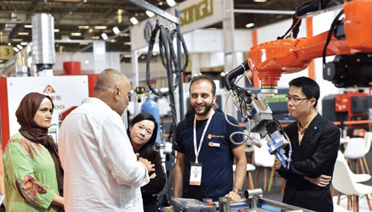 MAKTEK Avrasya fuarında bir stantta robotik uygulama başında bilgi alan ziyaretçiler