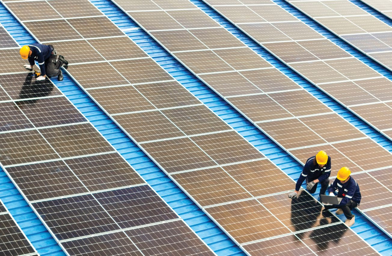Güneş enerjisi santralinde panel sıraları üzerinde çalışan bakım ekipleri