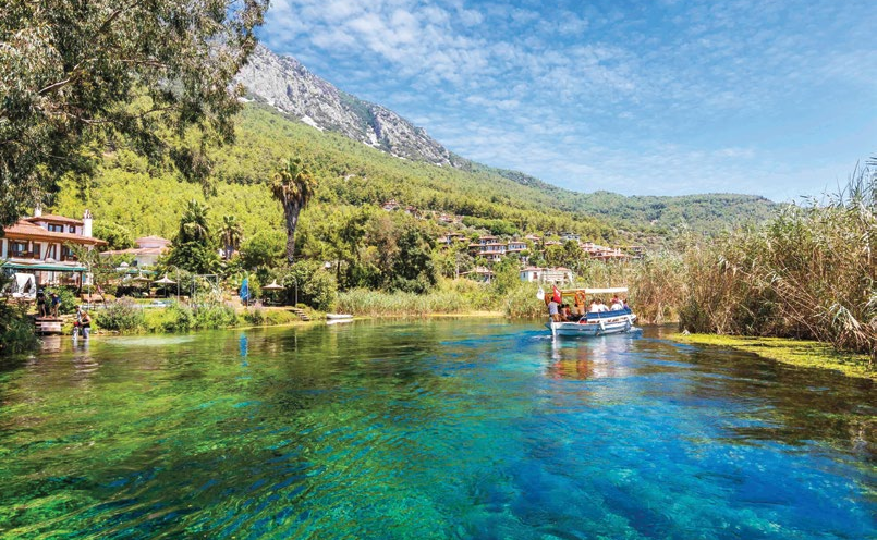 Muğla Akyaka'da Azmak Nehri'nin turkuaz suları, kıyıdaki restoranlar ve nehirde gezinti yapan tekne