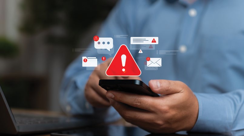Elinde akıllı telefon tutan bir kişi ve telefonun üzerinde beliren kırmızı ünlem işareti ile mesaj, e-posta, klasör ve uyarı bildirimi simgeleri
