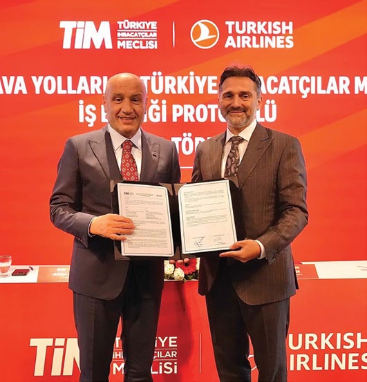 TİM ile Türk Hava Yolları iş birliği protokolü imza töreninde imzalanan protokolü birlikte gösteren iki kişi, arkada TİM ve Turkish Airlines logolu pano