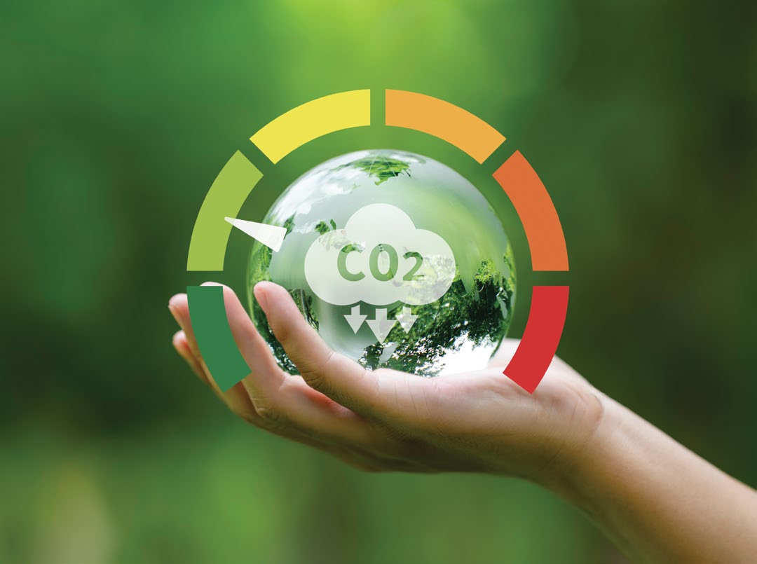 Avucunda, üzerinde CO2 bulutu simgesi bulunan cam küre tutan bir el; kürenin çevresinde yeşilden kırmızıya uzanan emisyon göstergesi